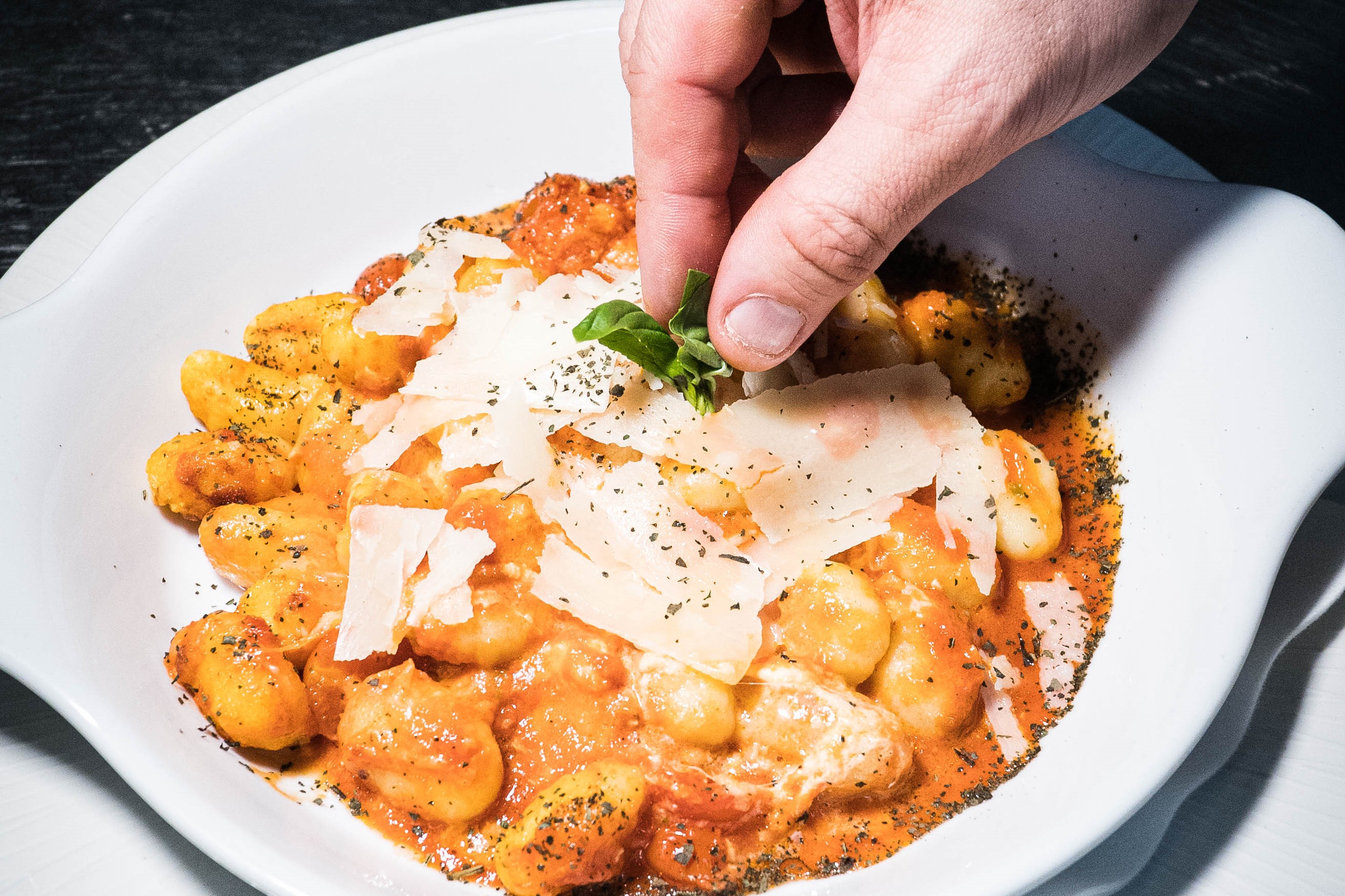A hand is putting parmesan on a plate of gnocchi