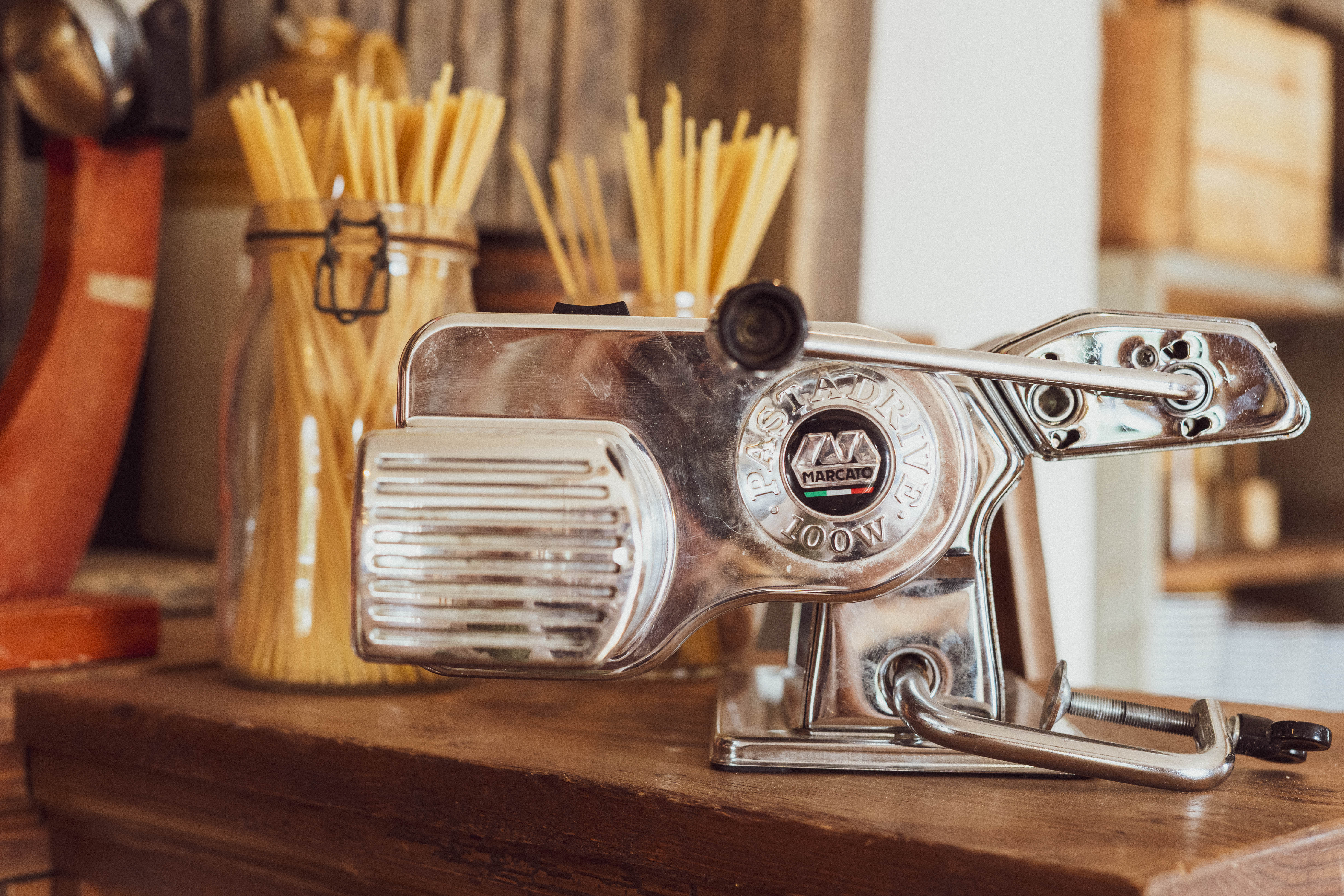 A metal pasta machine sits on top of a wooden table